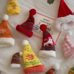 Flat lay of miniature knitted Christmas hats in various festive colors on white fabric