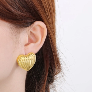 Close-up of 18K gold plated heart stud earrings with vertical striped texture on ear
