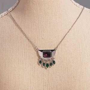 Detailed view of silver necklace with square purple stone and green teardrop gems