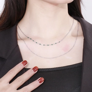 Close-up of double-layered silver cross chain with green resin beads on neck