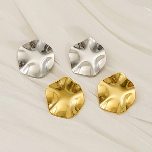 Detailed view of textured gold and silver disc earrings on white silk background