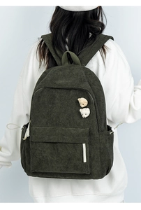 Detail eines grünen Cord-Rucksacks mit niedlichen Bären-Pins und praktischen Seitentaschen