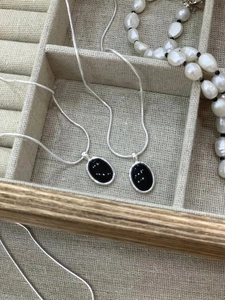 Detailed shot of two S925 silver necklaces with black oval onyx pendants on a linen tray