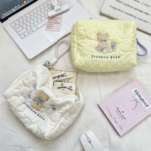 Macro detail of quilted makeup bag featuring cute bear embroidery and smooth zipper texture