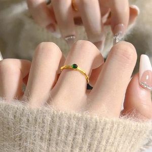 Close-up of bamboo-style gold ring with green gemstone on beige knit fabric