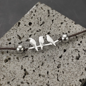 Macro shot of silver bird-themed bracelet with dark cord on natural stone surface