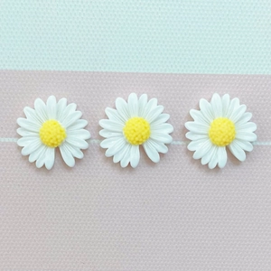 Close-up of three white resin daisy flower charms with yellow centers for DIY crafts