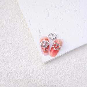 Close-up of silver hollow heart-shaped nail charms with rhinestones on white texture