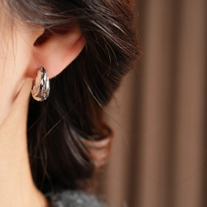 Detail of silver teardrop earrings with faceted cutting worn by a model in warm light