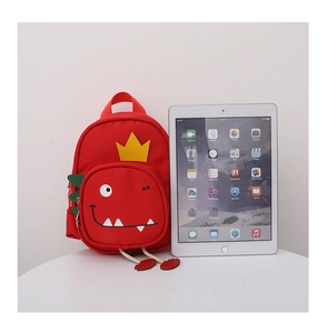Detail showing red canvas toddler dinosaur backpack with yellow crown next to a tablet