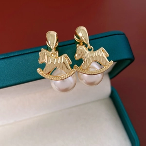 Détail de boucles d'oreilles cheval à bascule doré avec perles blanches sur un coffret bijoux