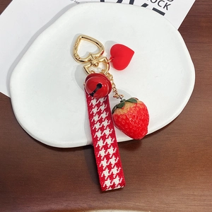 Detail of strawberry keychain with red bell and houndstooth ribbon on a white plate