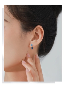 Detail of elegant silver stud earrings with square and round blue sapphire stones on model