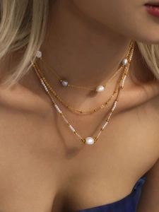 Dettaglio della collana a strati con catene d'oro e perle bianche e grigie sulla modella