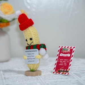 Handmade crochet banana doll with Christmas hat and scarf holding a motivational card