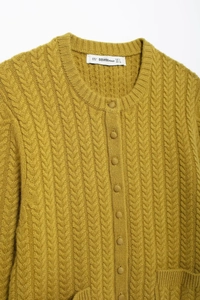 Detailed close-up of mustard yellow knitted cardigan showing cable weave and button closure