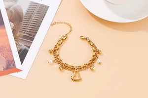 Détail d'un bracelet double rang doré avec pendentifs cœur et perles sur fond rose