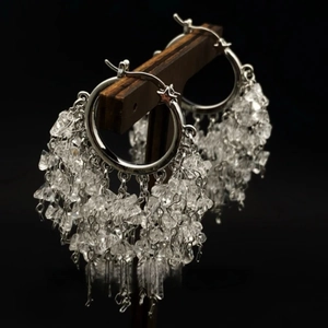 Close-up of silver hoop earrings featuring layered crystal tassels on a display stand