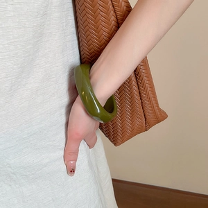 Detail of olive green acrylic chunky bangle on model wrist with stylish outfits