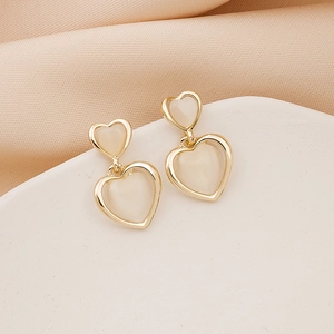 Macro detail of gold-plated double heart earrings with white cat eye stone inlays