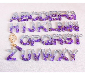 Detail view of 26 glitter resin alphabet keychains with purple tassels and gold accents