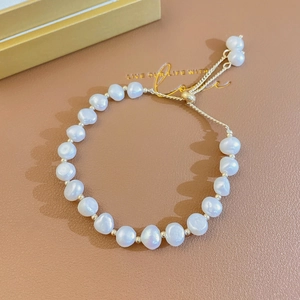 Macro detail of natural baroque pearl bracelet with gold hardware on brown leather