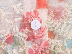 Macro shot of embroidery and floral print on sheer fabric with a white button detail