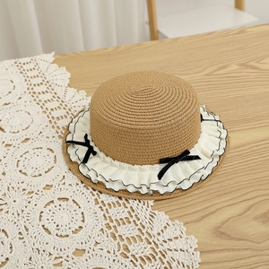 Detail of flat top straw hat featuring double-layer lace ruffles and black bow accents