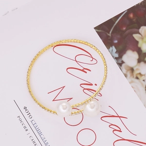 Close-up of gold open bracelet with two white pearls and sparkling rhinestone pavé setting