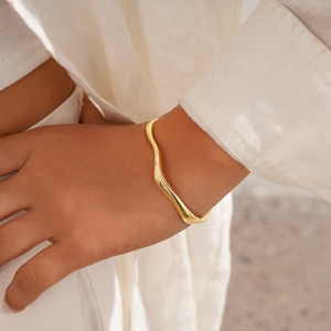 Detail of 18k gold-plated wavy cuff bracelet on woman's wrist with minimalist styling