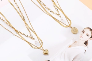 Détail d'un collier doré multicouche avec perles baroques, cœur et pendentif pièce