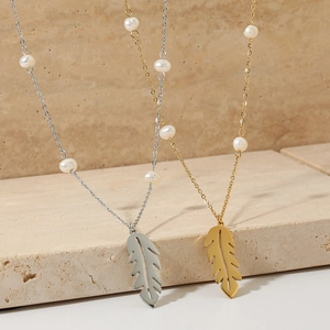 Elegant gold and silver feather pendant necklaces with pearls on a sandstone surface