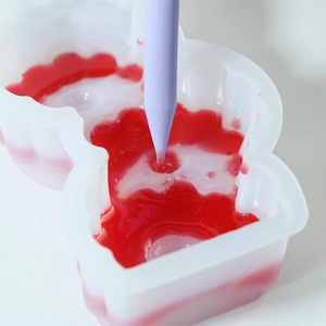 Detailed macro view of purple stir stick mixing red resin inside a silicone DIY mold