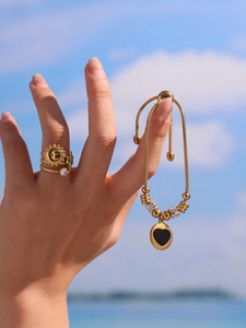 Détail du bracelet chaîne serpent doré avec breloque cœur noir et bagues motif soleil