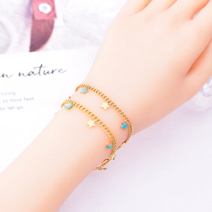 Double-layered gold chain bracelet with blue moon and star charms worn on wrist