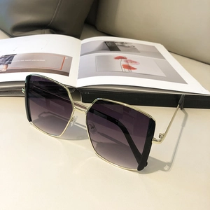 Detail view of square gold metal sunglasses with purple gradient lenses on a desk