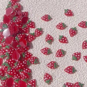 Vibrant resin strawberry nail art charms with green leaves on white textured surface