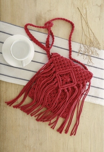 Detail einer roten Makramee-Umhängetasche mit Quasten auf Holztisch mit Kaffeetasse