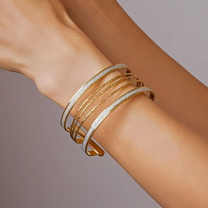 Detail shot of multilayered metallic bangles with gold textured rings and silver glitter finish