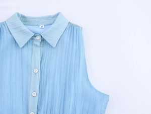 Detail of light blue sleeveless shirt dress featuring vertical stripes and white buttons