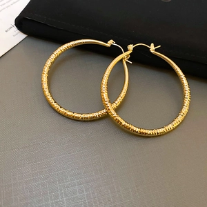 Macro detail of large golden hoop earrings with textured diamond-cut metal pattern