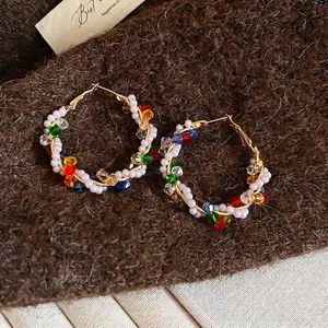 Colorful crystal and pearl wrap hoop earrings with gold metal on brown velvet