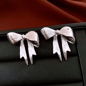 Macro shot of silver bow stud earrings with textured metallic finish on black velvet