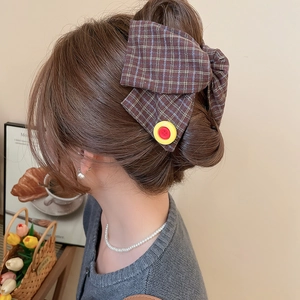 Close-up of brown plaid fabric bow hair clip with contrast button detail on model