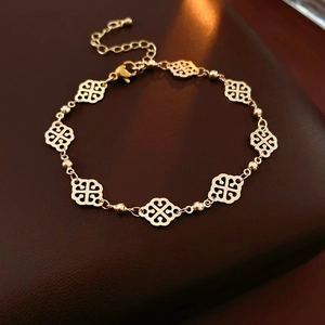 Detail of a gold clover-shaped hollow bracelet on a brown leather surface