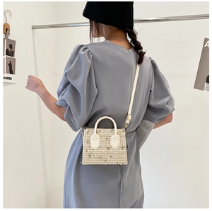 Detail of straw woven mini bag featuring floral embroidery and white leather handle