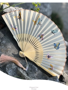 Macro detail of silk folding fan featuring vibrant butterfly embroidery and long tassel