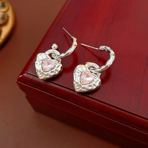 Detailed shot of silver heart earrings with pink gemstones on a red wooden jewelry box