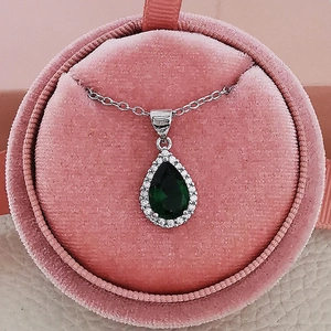 Close-up of a pear-shaped silver necklace with a green zircon in a pink velvet jewelry box