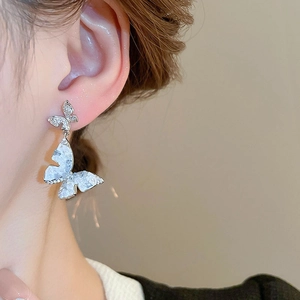 Detailed close-up of butterfly earrings with rhinestones and white marble texture